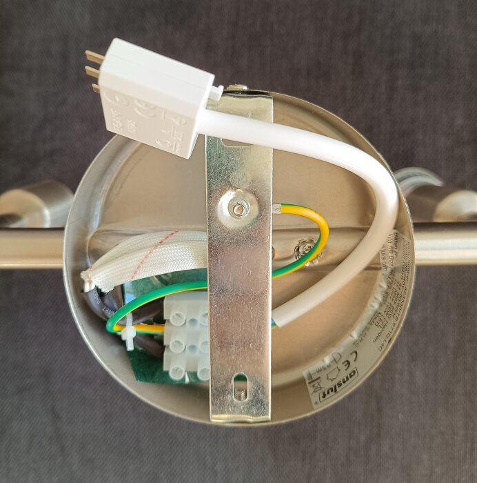 Botten av en taklampa med synliga elkontakter och kablar, monterad på en metallplatta, avsedd för installation.