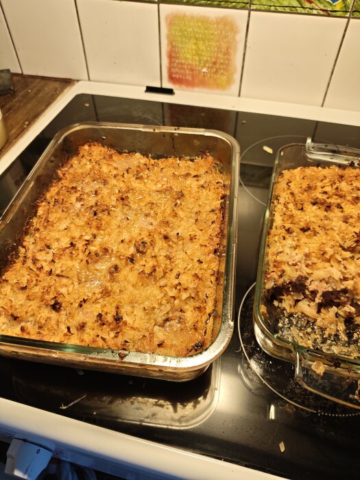 Kålpudding i två ugnsformar på en spis, med gyllenbrun yta och rikligt med kål och köttfärs.