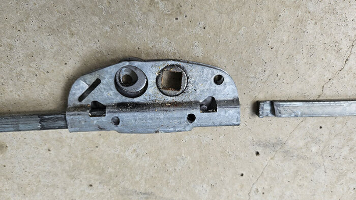 Gammal spanjolett i metall med rost och smuts, liggande på en betongyta. En skena är lossad och synlig vid sidan.