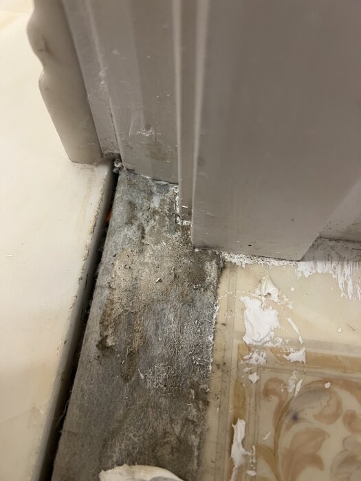 Tätskikt skuret mot dörrkarm under tröskeln, nivå en bit under marmorns ovansida, med synlig fogmassa runtom.