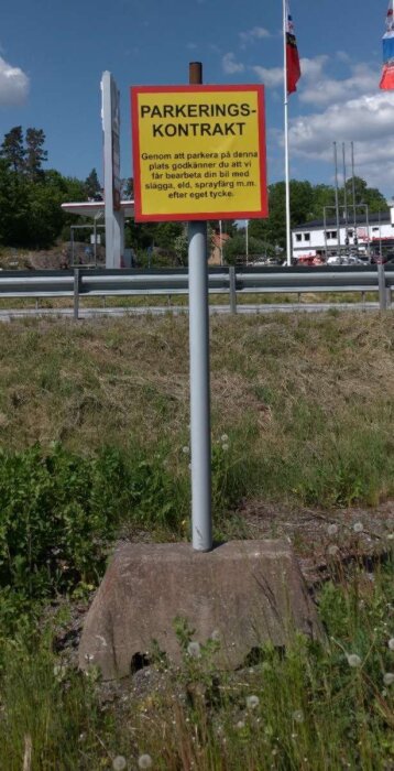 Skylt vid parkering med varningstext om att bilar kan bearbetas med slägga, eld och sprayfärg. Gräs och flaggor i bakgrunden.