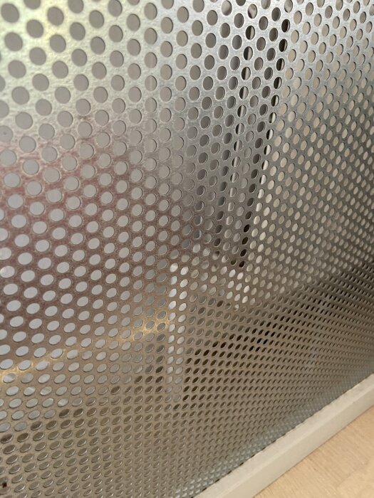 Perforerad metallpanel framför värmesystem, kan indikera typ av radiator för diskussion om uppvärmningsalternativ som luft/vatten eller bergvärme.