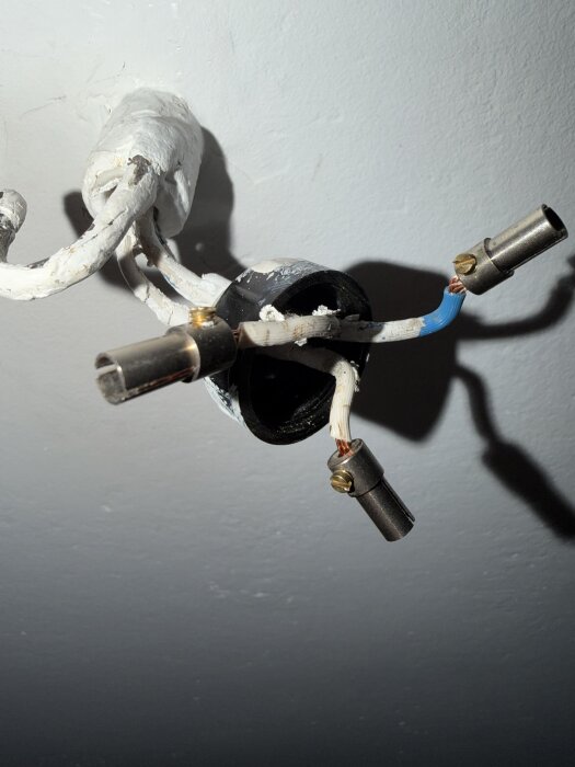 Två vita elkablar i taket med metalliska anslutningar, en blå neutral kabel synlig, stickkontakt för belysning.