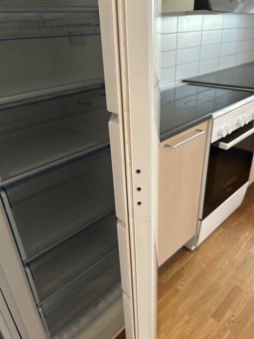 Öppen dörr till ett Bosch kylskåp utan handtag, i ett kök med trägolv och spis.