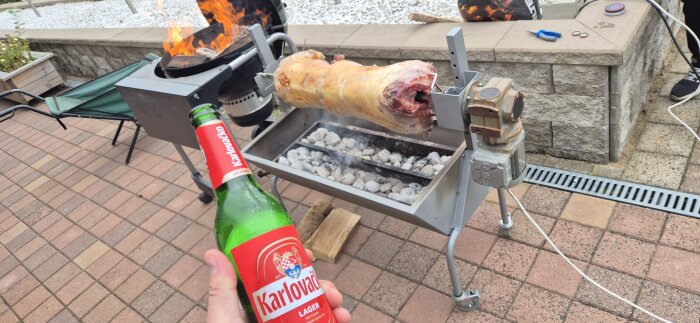 Grillning av lamm över kol, eld i bakgrunden och en hand som håller en flaska Karlovačko öl.