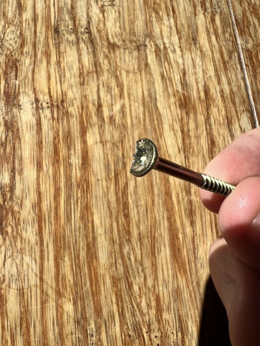 Skruv med ett djupt jack, hållen i en hand, mot en träyta. Skadorna orsakades vid fräsning i golvprojekt.