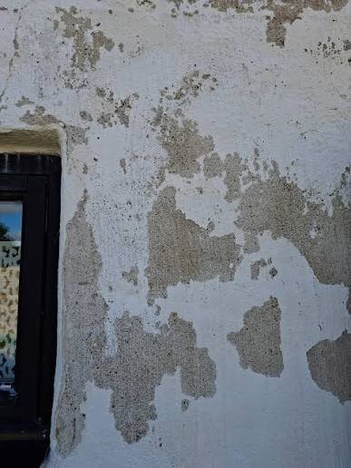 Flagnande kalkfärg på en vägg bredvid ett fönster.