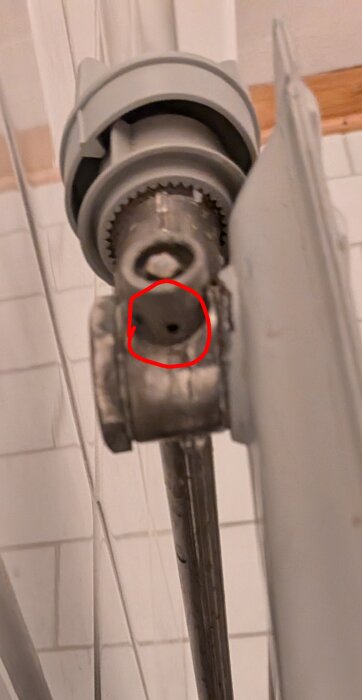 Närbild av skadad och läckande avluftningsventil på en radiator. Ventilens kvadratiska skruv är deformerad med ett rödmarkerat läckagehål.