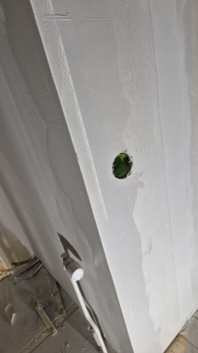 Spacklad gipsskiva med grönt hål för eluttag och en tillhörande vit slang i ett utrymme under renovering.