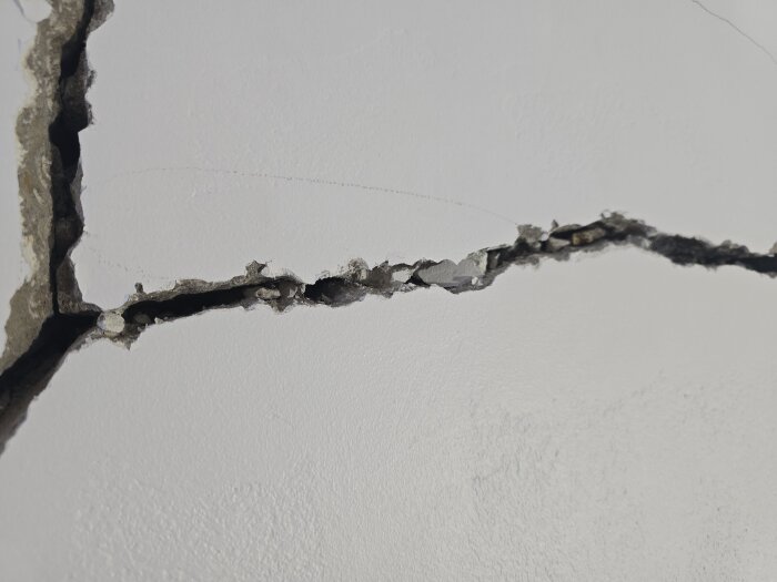 Sprickor i en vägg med delvis exponerat och skadat material, visar strukturella skador inför renovering.