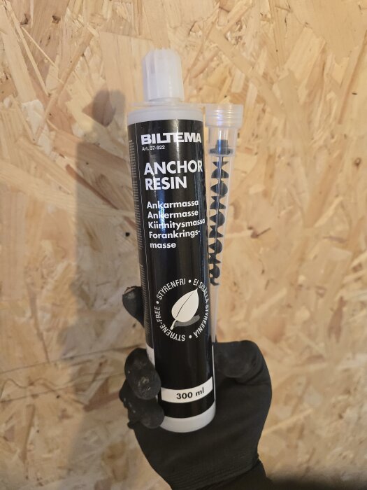 Biltema ankarmassa, 300 ml, i en svart förpackning med texten "Anchor Resin" och olika språk, hålls av en hand i en svart handske.