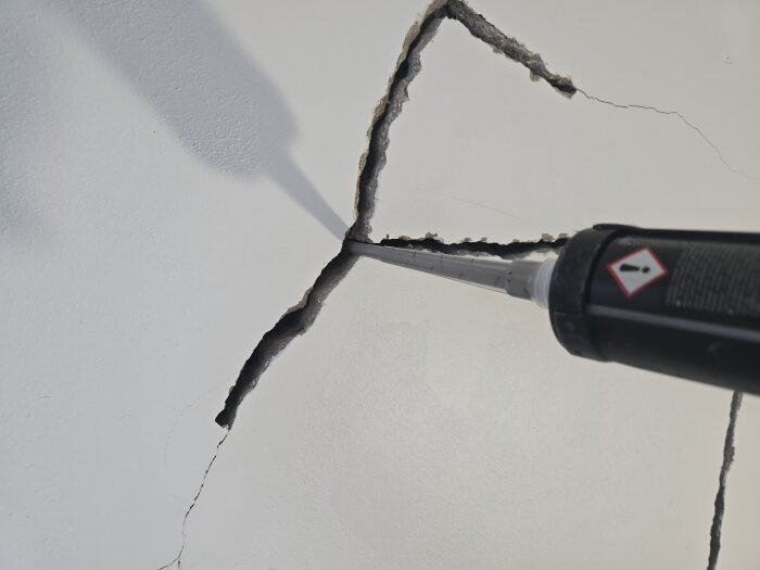 Närbild av en sprucken vägg där ankarmassa appliceras med en fogpistol för att laga sprickorna.