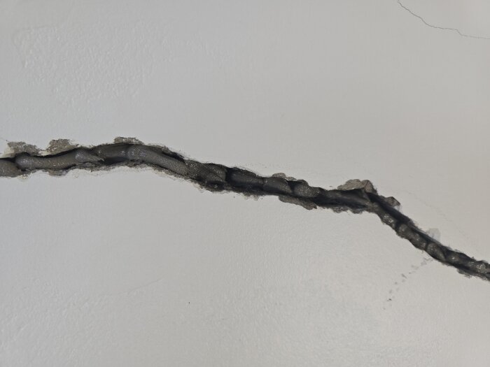 Spricka i vägg fylld med ankarmassa för renovering; detalj av pågående reparationsarbete i källare där sprickan tidigare orsakats av svag betong.