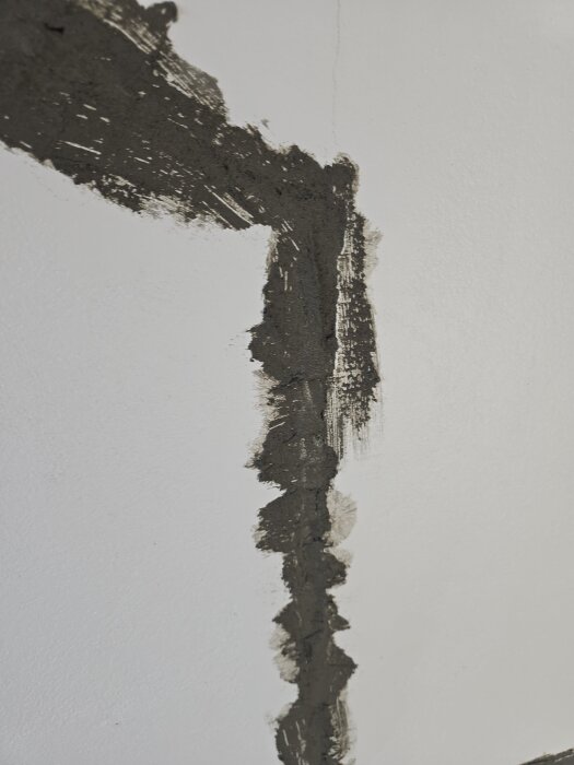Vägg med pågående reparation av spricka, täckt med mörkt lagningsbruk applicerat på en vitmålad yta i en källarrenovering.