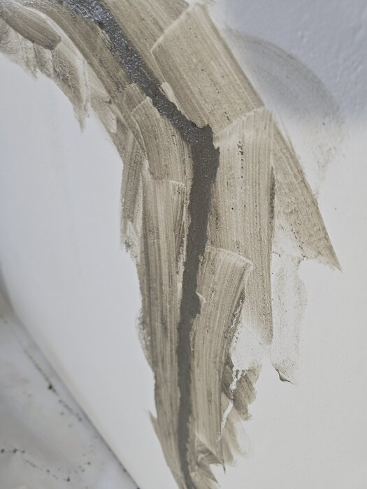 Spricka i en vit vägg lagad med ankarmassa och lagningsbruk, med tydliga märken av spackel och pågående renovering.