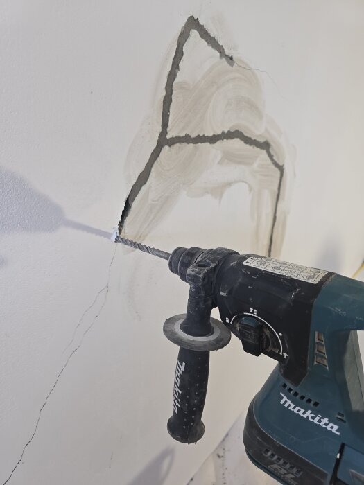 Borrmaskin borrar i vägg med sprickor för reparation i renoveringsprojekt.
