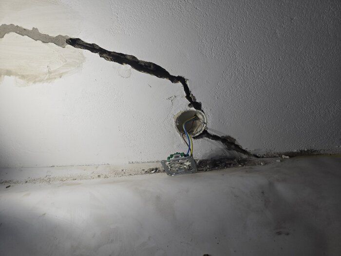 Sprucken vägg med synliga elledningar från en eldosa, omfattande sprickor som sträcker sig genom betongputsen i ett renoveringsprojekt.