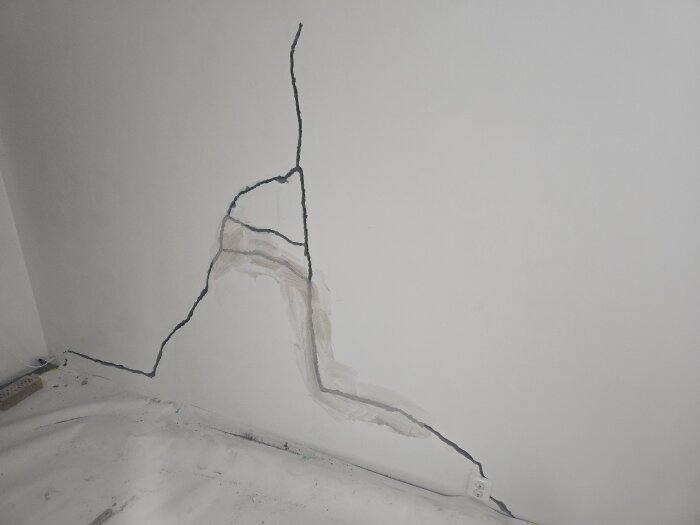 Sprucken vägg i källarens sovrum, delvis reparerad med lagningsbruk och ankarmassa synlig. Golv täckt med skyddspapp.