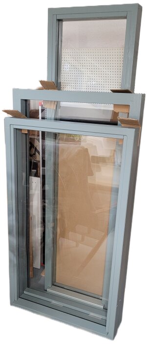 Tre gröna fönster med glas, lutade mot en vägg. Används för fristående förråd.