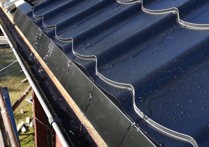 Svart plåttak med regndroppar, vatten rinner ner mot hängränna. Visar nyinstallerat tak med vattendränering.