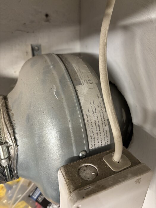 Ventilationsfläkt från cirka 2010 monterad i ett hus, med elkabel och väggfäste synliga.