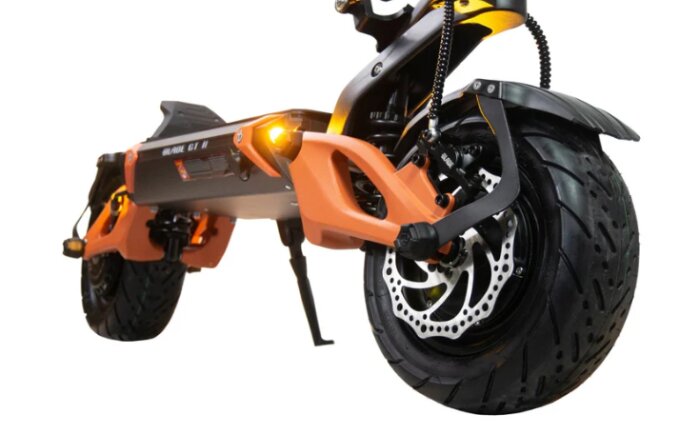 El-scooter med robusta hjul och diskbromsar, troligtvis av hög kvalitet, fotad från sidan med fokus på framhjulet och orange detaljer.