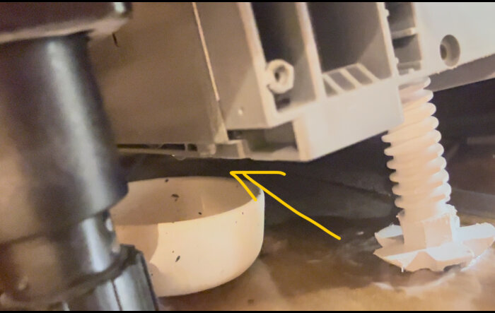 Närbild på undersidan av diskmaskin med gul pil som markerar möjlig läckagepunkt, vatten på golvet och en vit skål under.