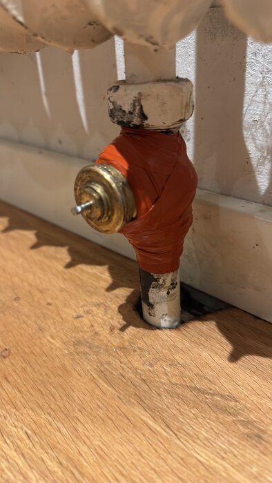 Litet rör anslutet till ett element, inlindat i orange självvulkaniserande tejp för att åtgärda en vattenläcka, mot träbakgrund.