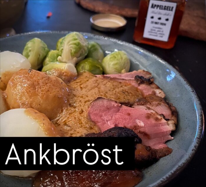 Ankbröst med kokt potatis, brysselkål och pepparsås på en tallrik. I bakgrunden syns en burk äppelgelé med chili.