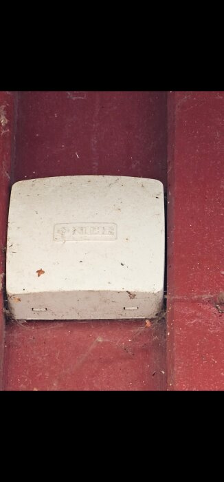 Vit utegivare från NIBE monterad på en röd fasad.