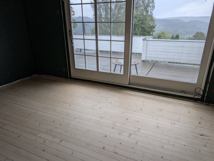Nyrenoverat trägolv i ljust trä med få springor, beläget i rum med stora fönster och utsikt mot veranda och grönskande landskap.
