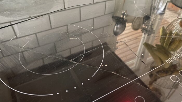 Sprucken induktionshäll med tydlig spricka över ytan i kök.