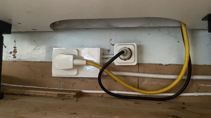 Eluttag under diskbänk med en gul kabel kopplad i vänster uttag och en svart kabel i höger uttag, träpanel i bakgrunden.