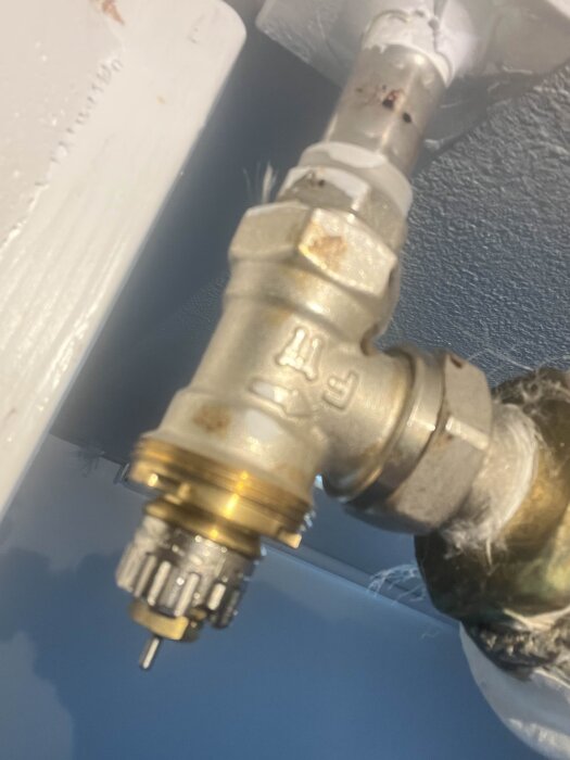 Radiatorventil med metallkoppling och synliga skruvar, liknande en Danfoss RAN, monterad mot vägg.