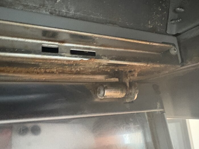 Rostig skruv och räfflad mutter under en köksfläkt, svårtillgänglig och svår att ta bort för rengöring bakom fästet.