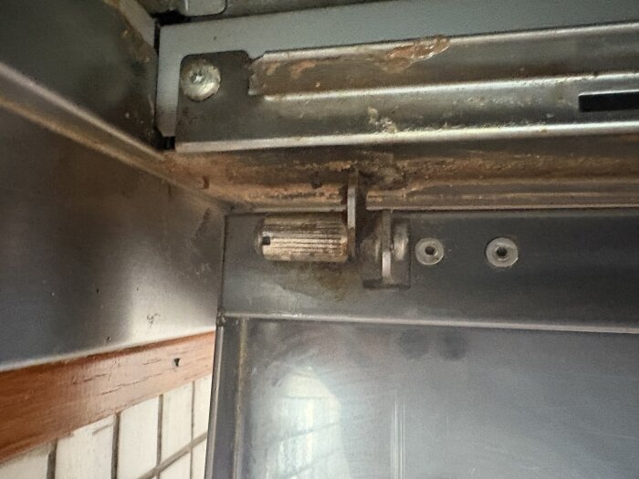 Närbild på en köksfläktluckas fäste, med en svåråtkomlig skruv och räfflad mutter i hörnet av metallramen.
