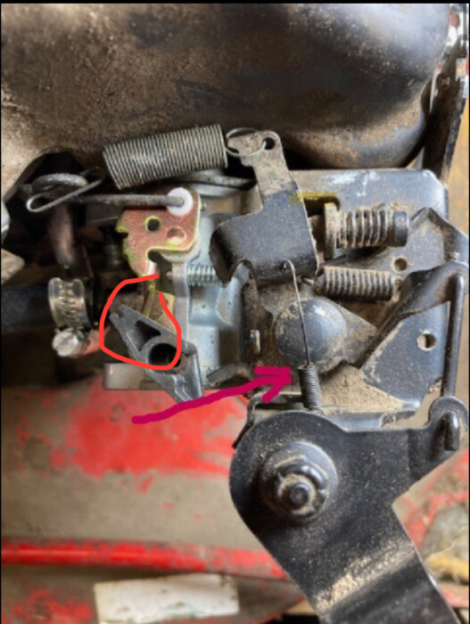 Fjäder för choken markerad med röd cirkel och rosa pil på motordel.