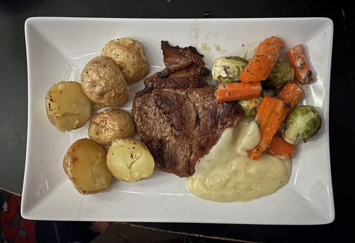 Fläskkarré med ugnsstekt potatis, brysselkål och morot på tallrik, serverat med sås.