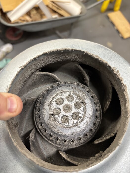 Dammig fläkt med flera blad, hållen av en hand. En skottkärra med byggmaterial syns suddigt i bakgrunden.