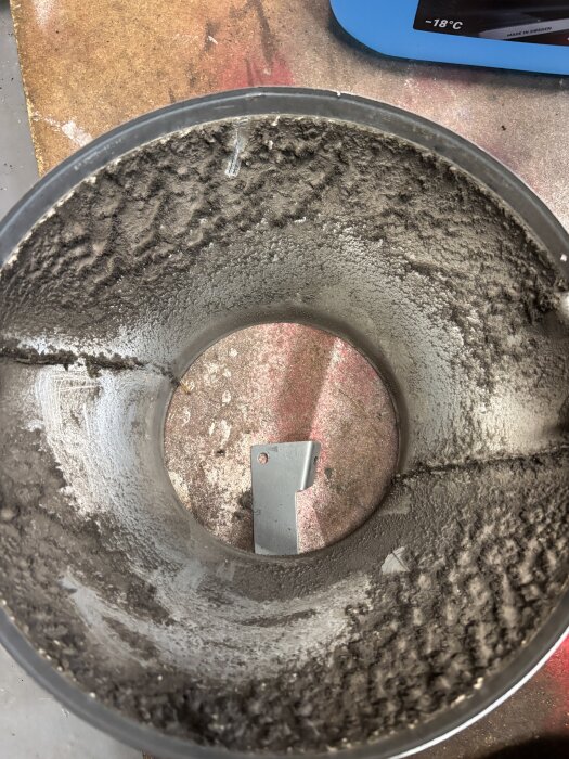 Utsikt av insidan på ett dammigt metallrör med smutsavlagringar. Bakgrunden visar ett rostigt golv och en blå maskin.