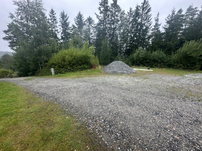 Grusplan omgiven av skog, med en hög grus i bakgrunden och grönska på sidorna.