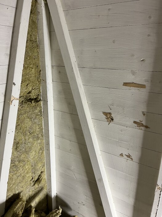 Isolerad innervägg i ett rum med vitmålad träpanel och delvis synlig gul isolering.