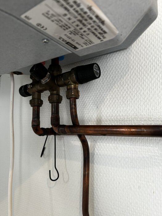 Ventil och kopparrör under en enhet, troligen en del av ett VVS-system. Tillhör en NIBE EVH 15-55CU, med text på panelen ovanför.