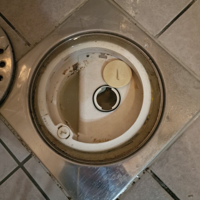 Avlopp med avlägsnat skruvlock, synligt runt hål för rengöring i äldre hus.