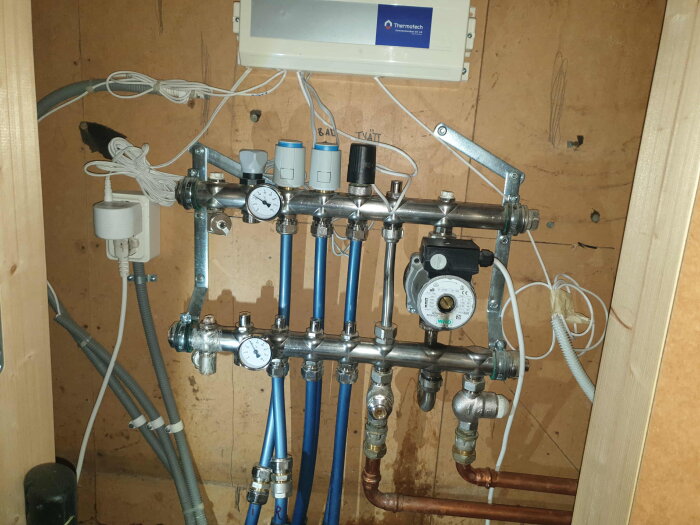 System för golvvärme med mätare och kopplingar, inklusive en cirkulationspump.