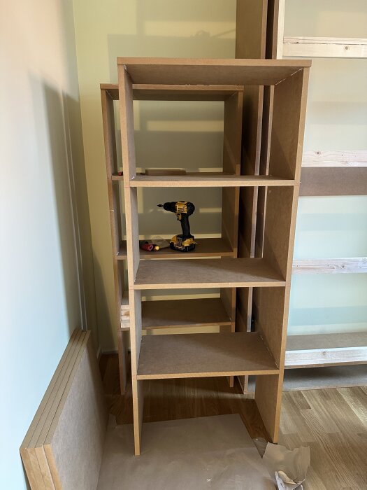 MDF-hyllor under konstruktion, med en borrmaskin placerad på en av hyllplanen, del av ett projekt för att bygga ett sängskåp med lagring.