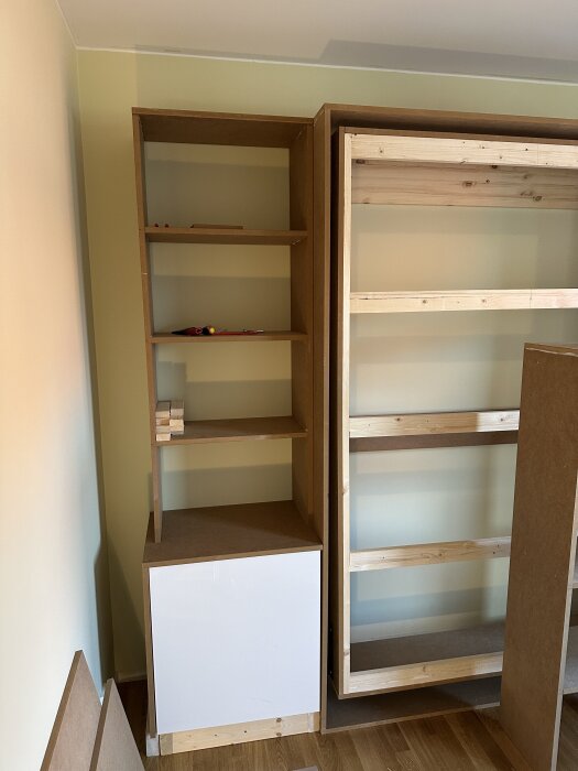 Hylla och stomme av trä monteras vid sängskåpsprojekt i gästrummet. MDF och IKEA-stomme används, halvfärdiga utan sockel och knoppar.