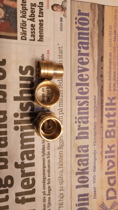 Tre kopparfärgade kopplingar placerade på en tidning, med frågan om det är en klämringskoppling till 16mm sidan.