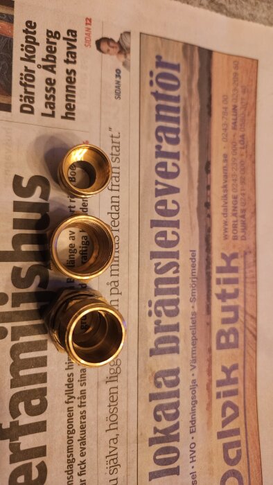 Tre rörkopplingsdelar ligger på en dagstidning, ifrågasatta som klämringskoppling för 16mm rör utan synlig klämring.