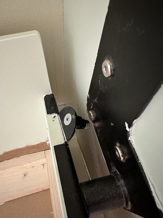 Närbild på beslag och fäste till ett sängskåp, med synliga skruvar och metalldelar, i ett pågående byggprojekt.